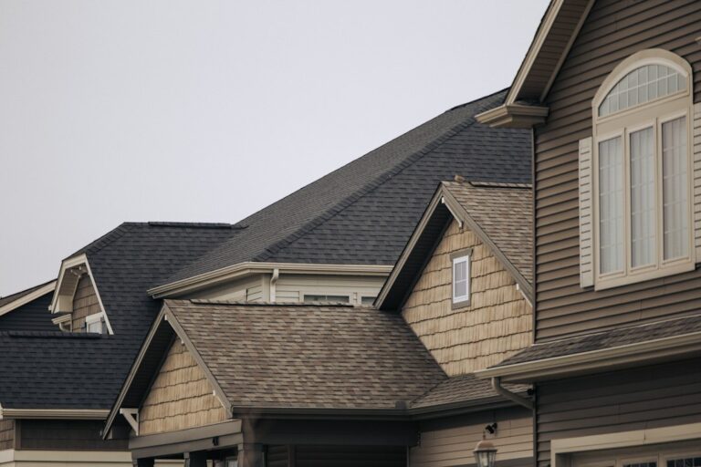 Roofing samples are arranged beside siding and trim on a residential home exterior in natural daylight.